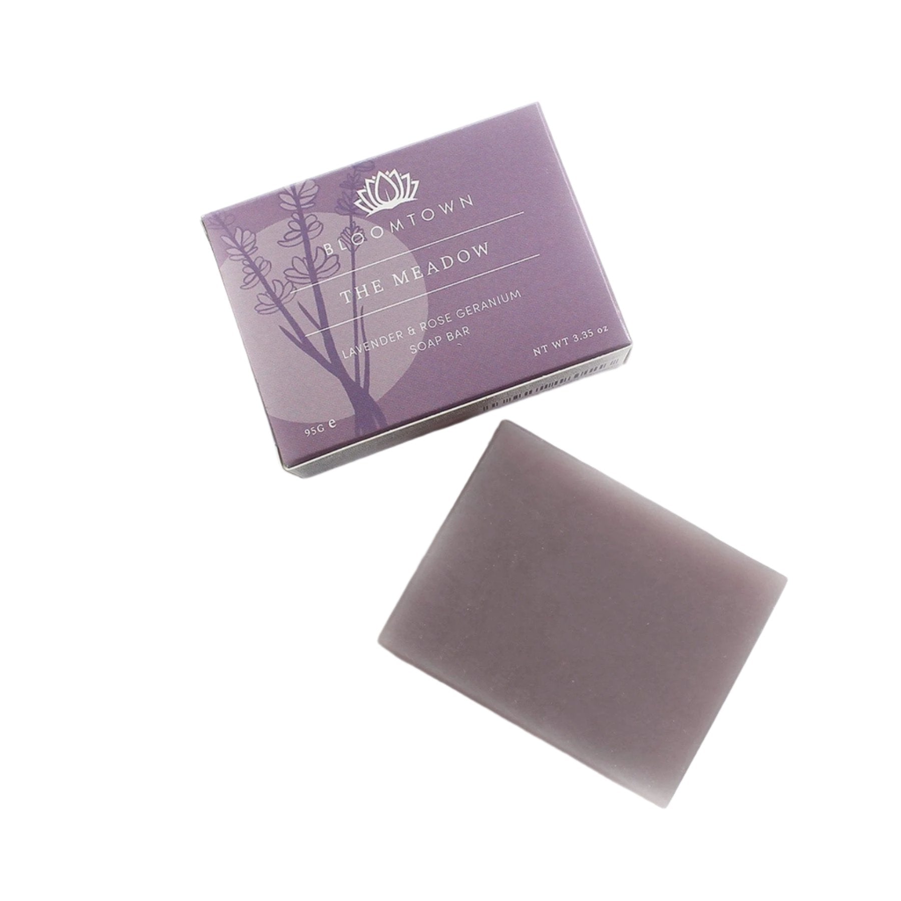 Lavender and rose geranium soap bar next to its purple packaging with botanical illustration, Bloomtown brand "The Meadow" organic and vegan skincare, white background.