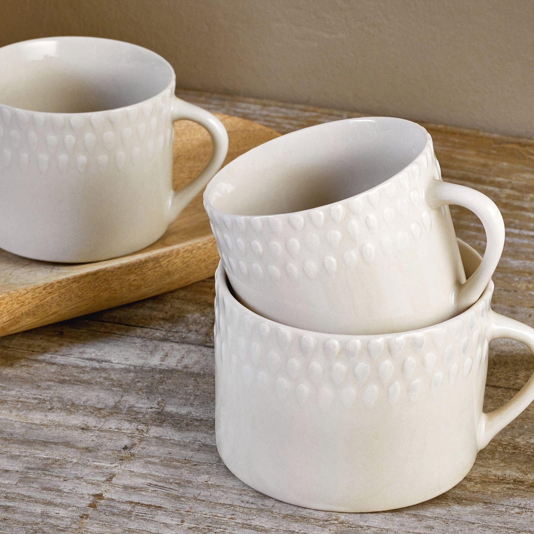 Three white textured ceramic coffee mugs stacked on a wooden surface with a wooden spoon in the background.