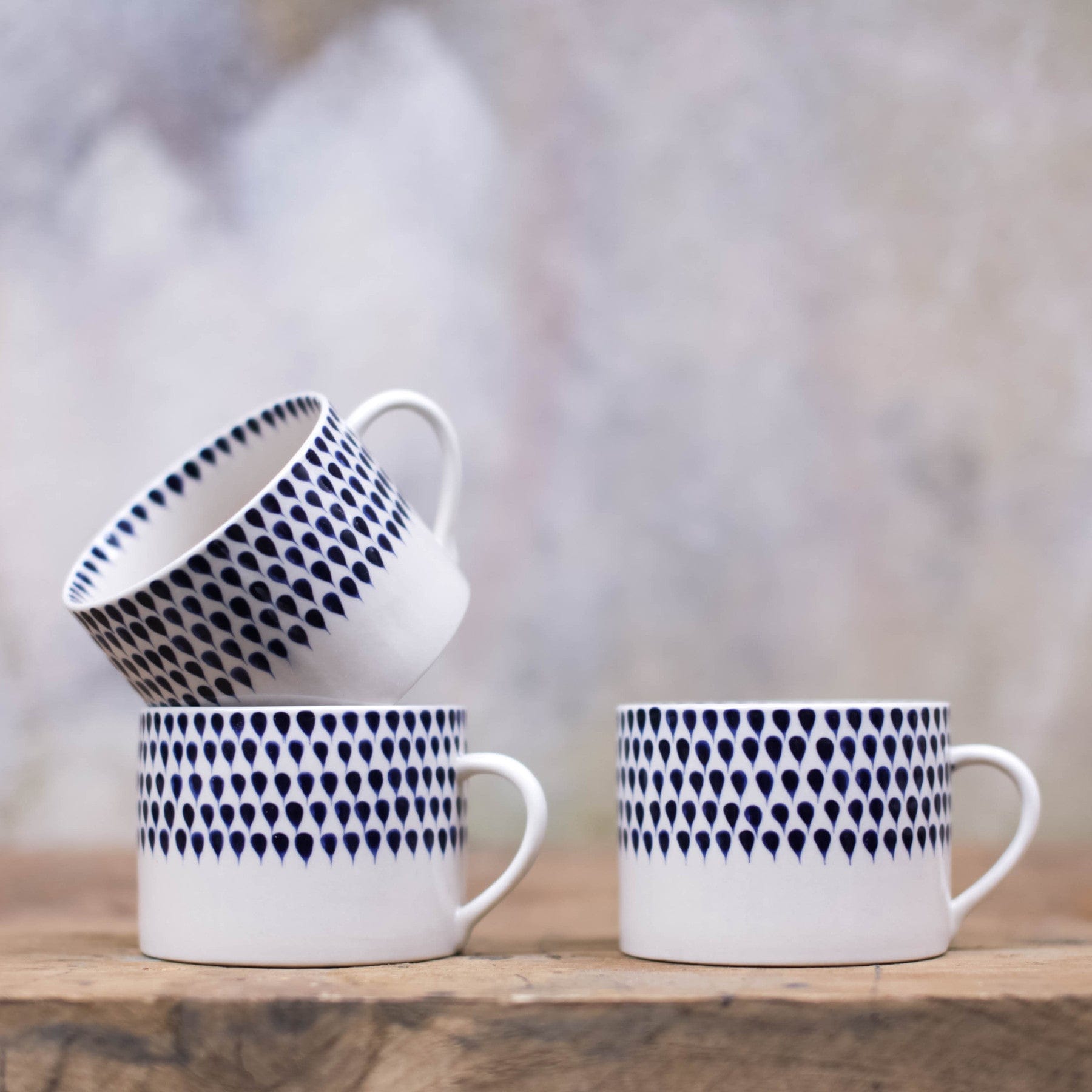 Stacked and side-by-side white ceramic cups with blue teardrop patterns on wooden surface against a textured grey background