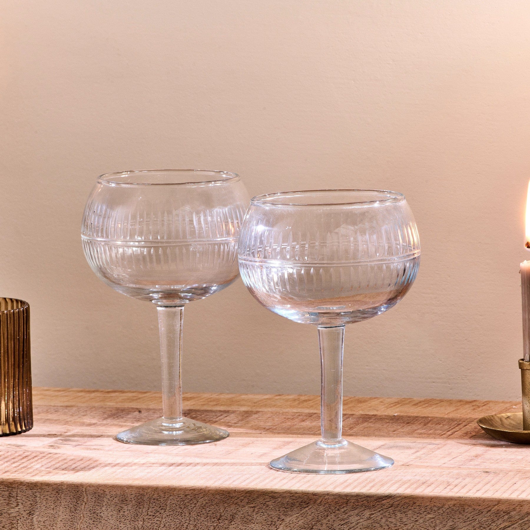 Two empty ribbed glass goblets on wooden surface with warm ambient lighting and candle in background.