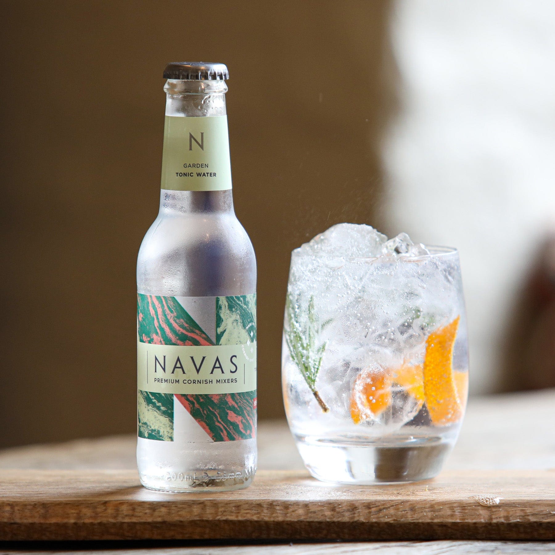 Navas Garden Tonic Water bottle beside glass with ice cubes and citrus garnish on wooden surface