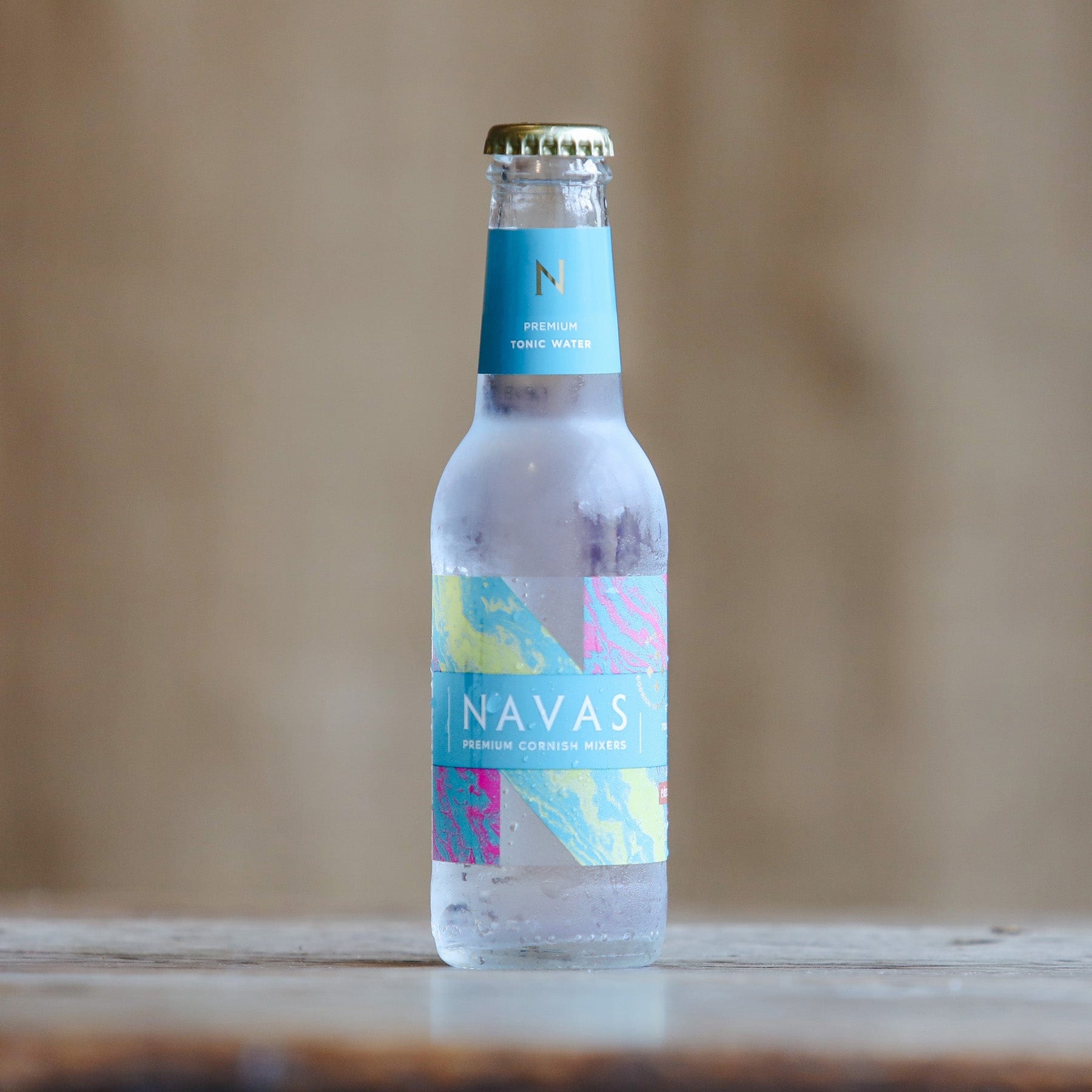 Condensation-covered Navas premium tonic water bottle on wooden surface with colorful label design, beverage product photography, focused and well-lit with soft background