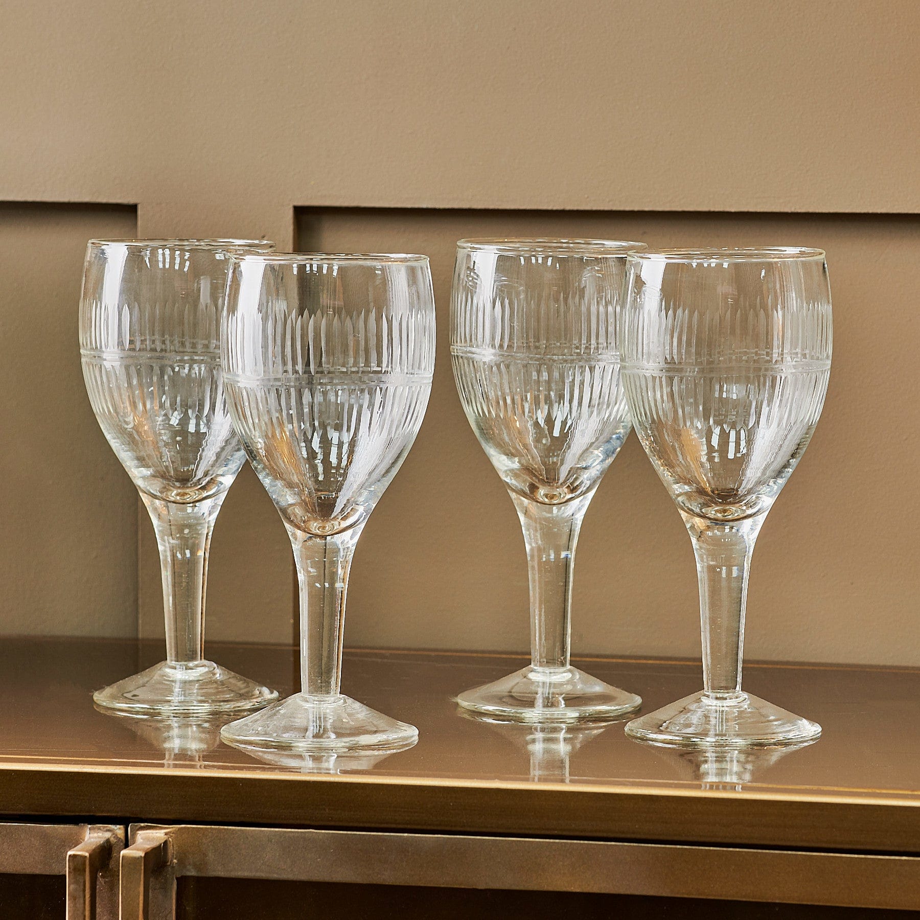 Four elegant wine glasses on a reflective surface with a neutral colored background