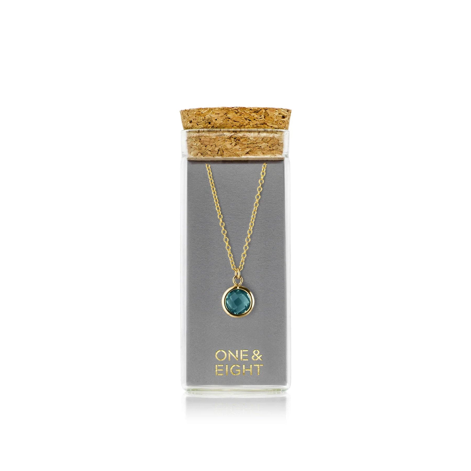 Elegant gold necklace with teal pendant presented in a transparent glass jar with cork top on white background.