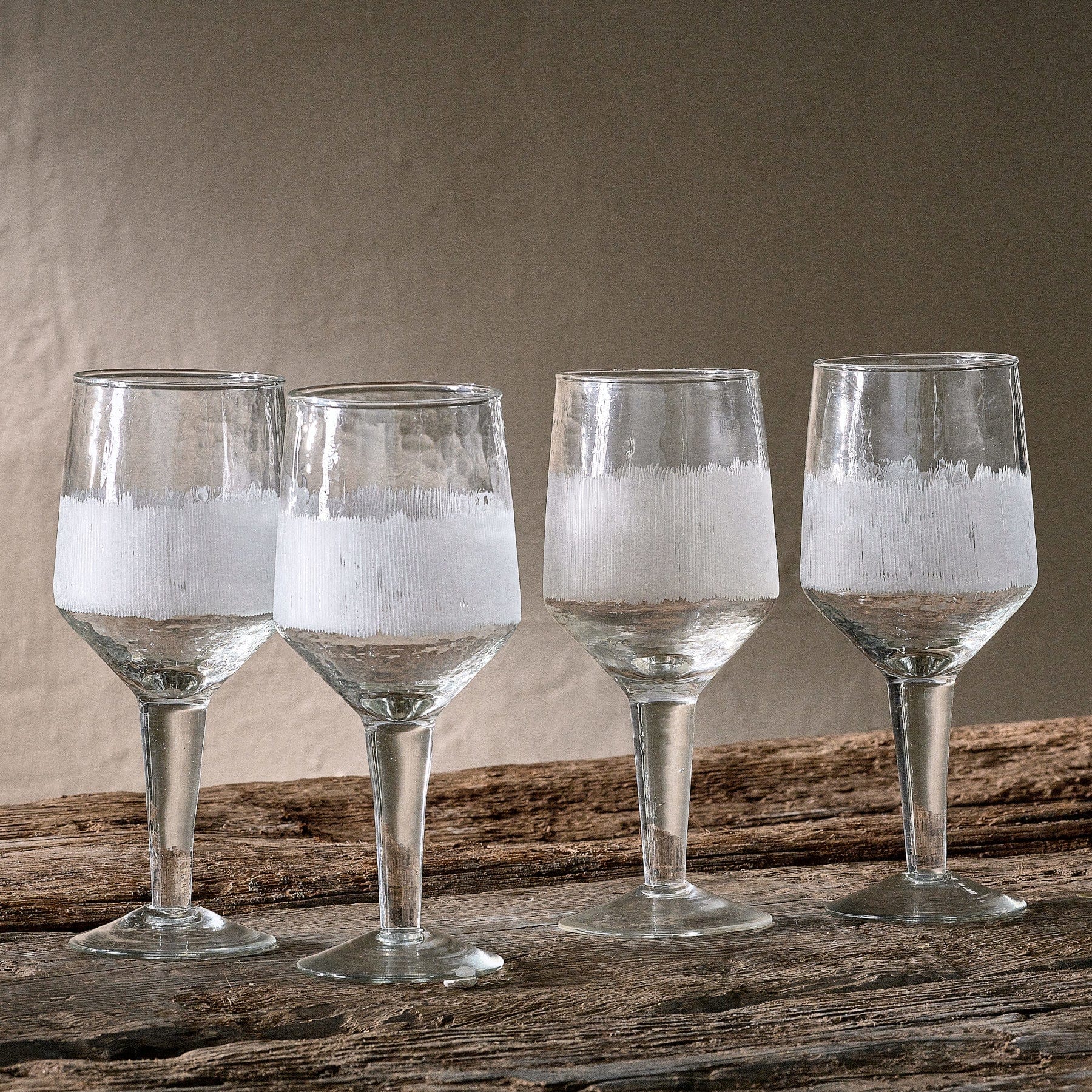Four wine glasses with water on rustic wooden table against neutral background, glasses with condensation, still life, glassware concept