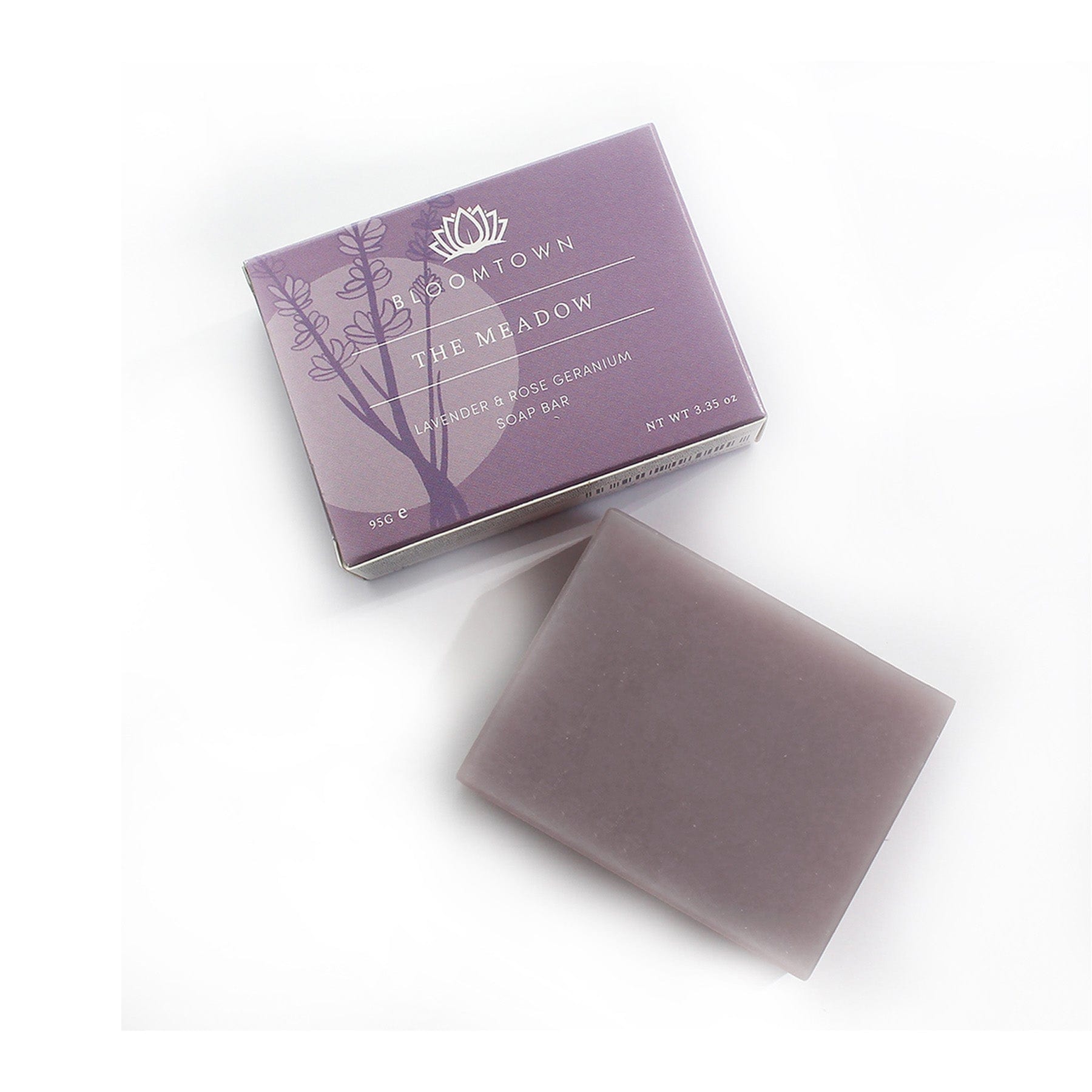 Lavender and rose geranium soap bar next to its purple packaging with botanical illustration, Bloomtown brand "The Meadow" organic and vegan skincare, white background.