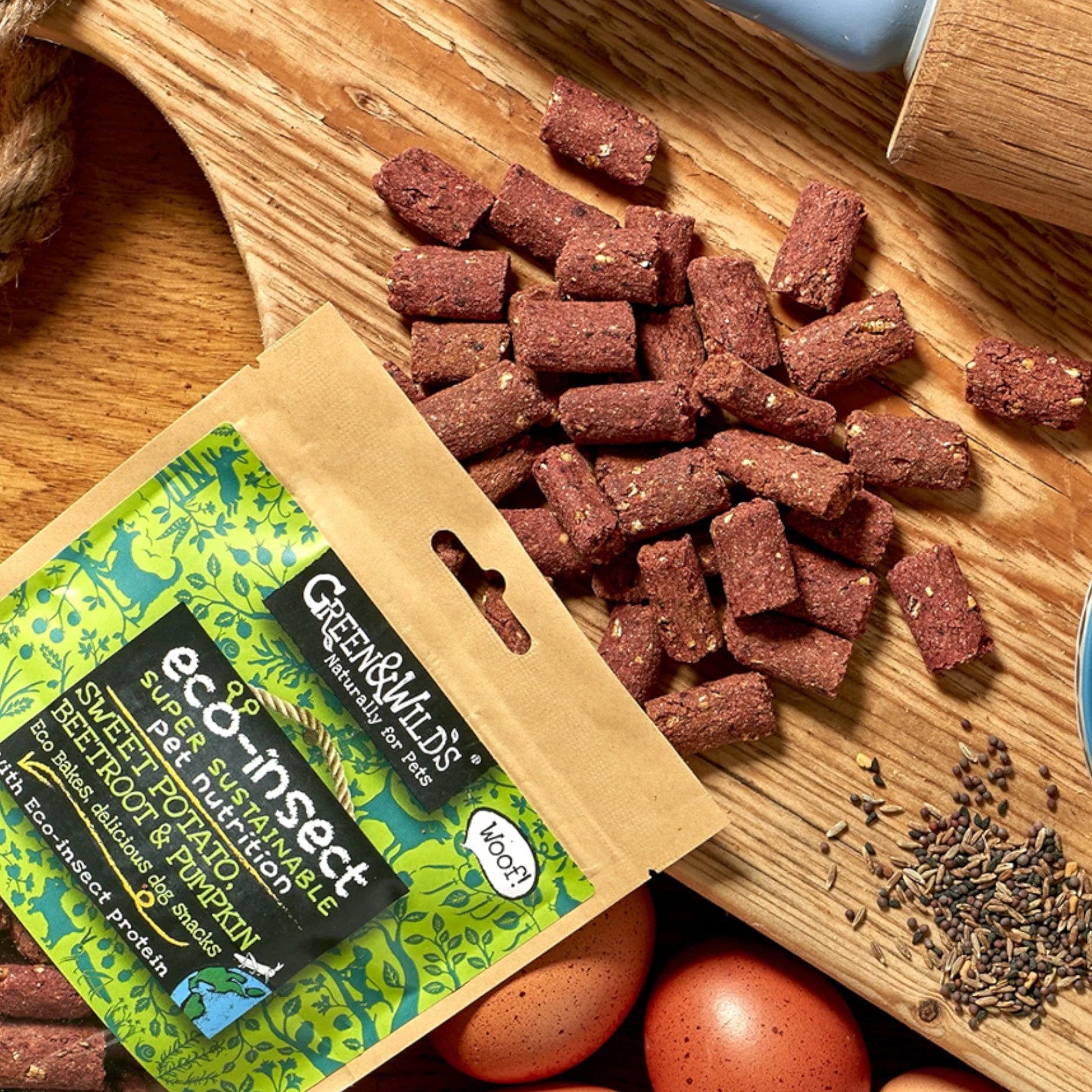 Eco-friendly insect protein dog treats spilling from a sustainable packaging on wooden surface next to eggs and a scoop of seeds.