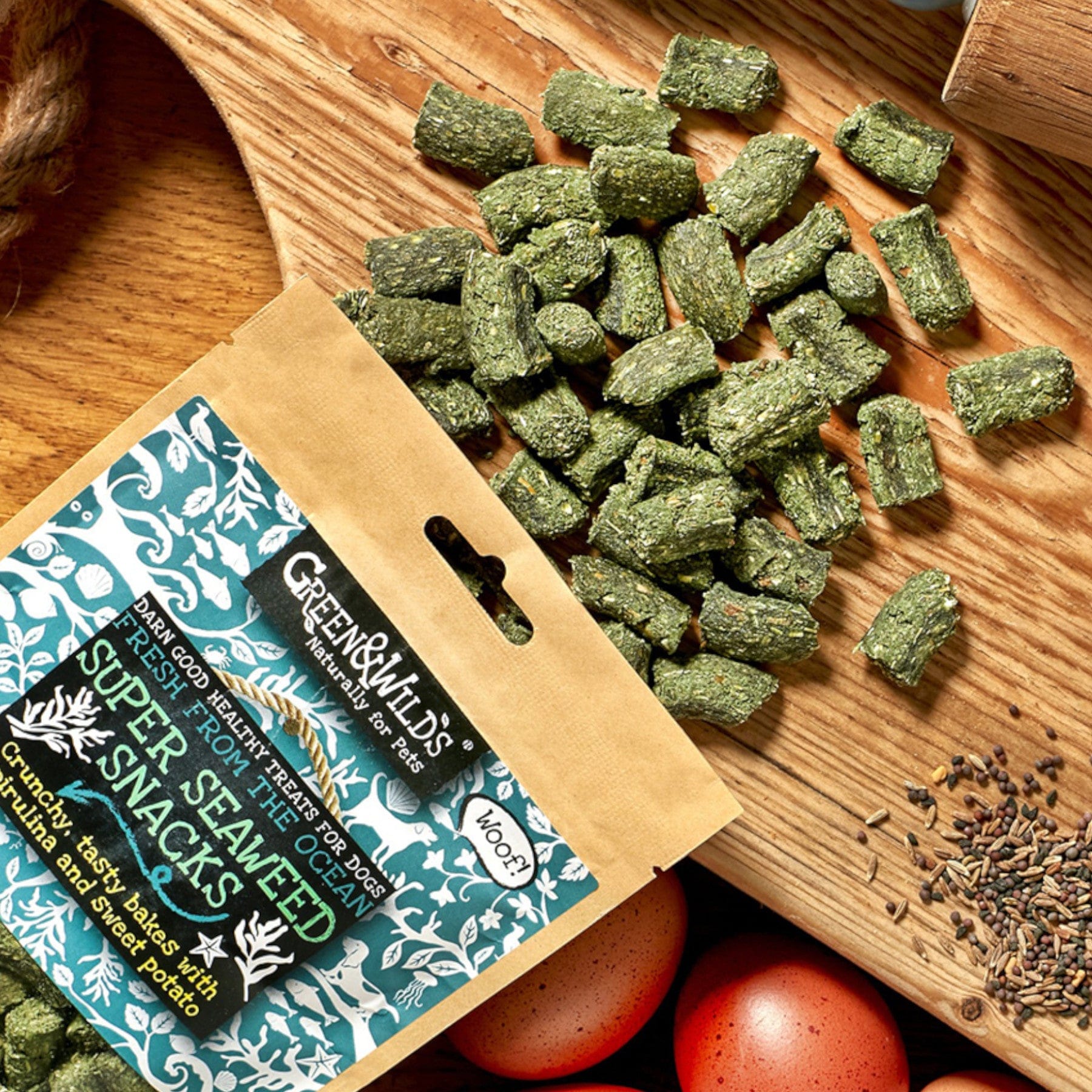 Organic Green & Wilds Super Seaweed Snacks packaging and scattered crunchy treats on wooden surface with brown eggs and jute bag visible.