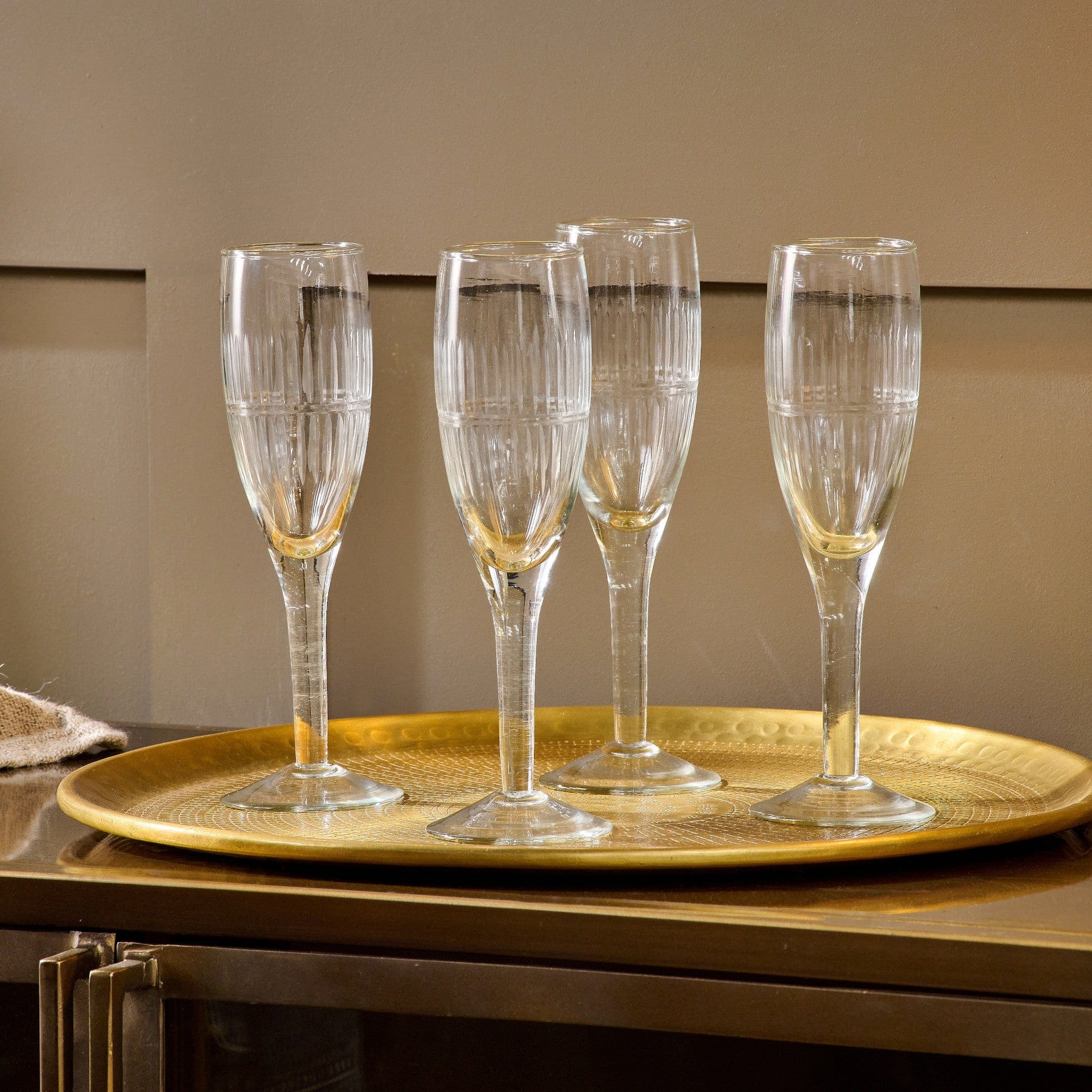 Elegant champagne flutes on a golden tray with subtle reflections, set against a neutral brown background