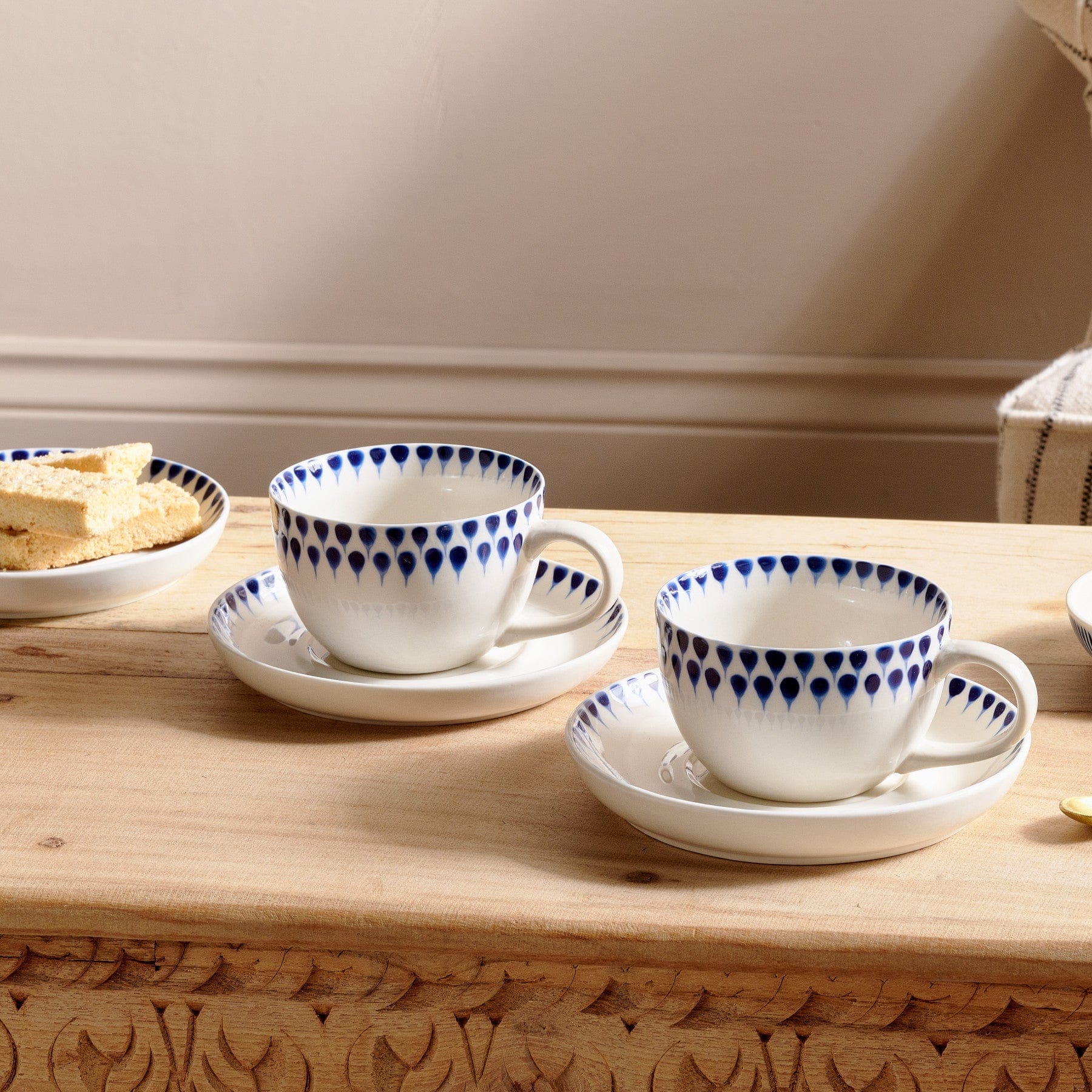 Elegant white and blue teacup sets on wooden table with matching saucers, plate of biscuits, cozy home breakfast scene.