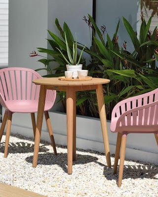 Modern outdoor patio with pink chairs, wooden round table, decorative succulent plant, gravel flooring, and tropical plants in background