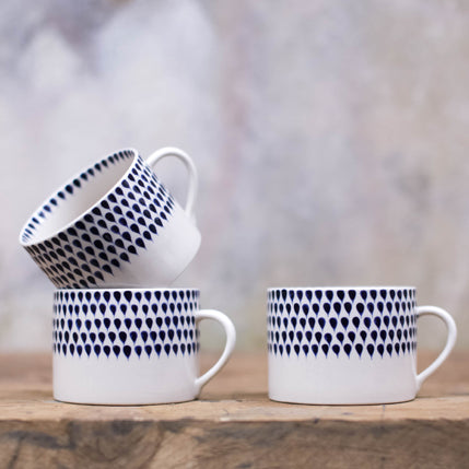 Ceramic coffee mugs with blue teardrop pattern stacked on a wooden surface with a blurred background